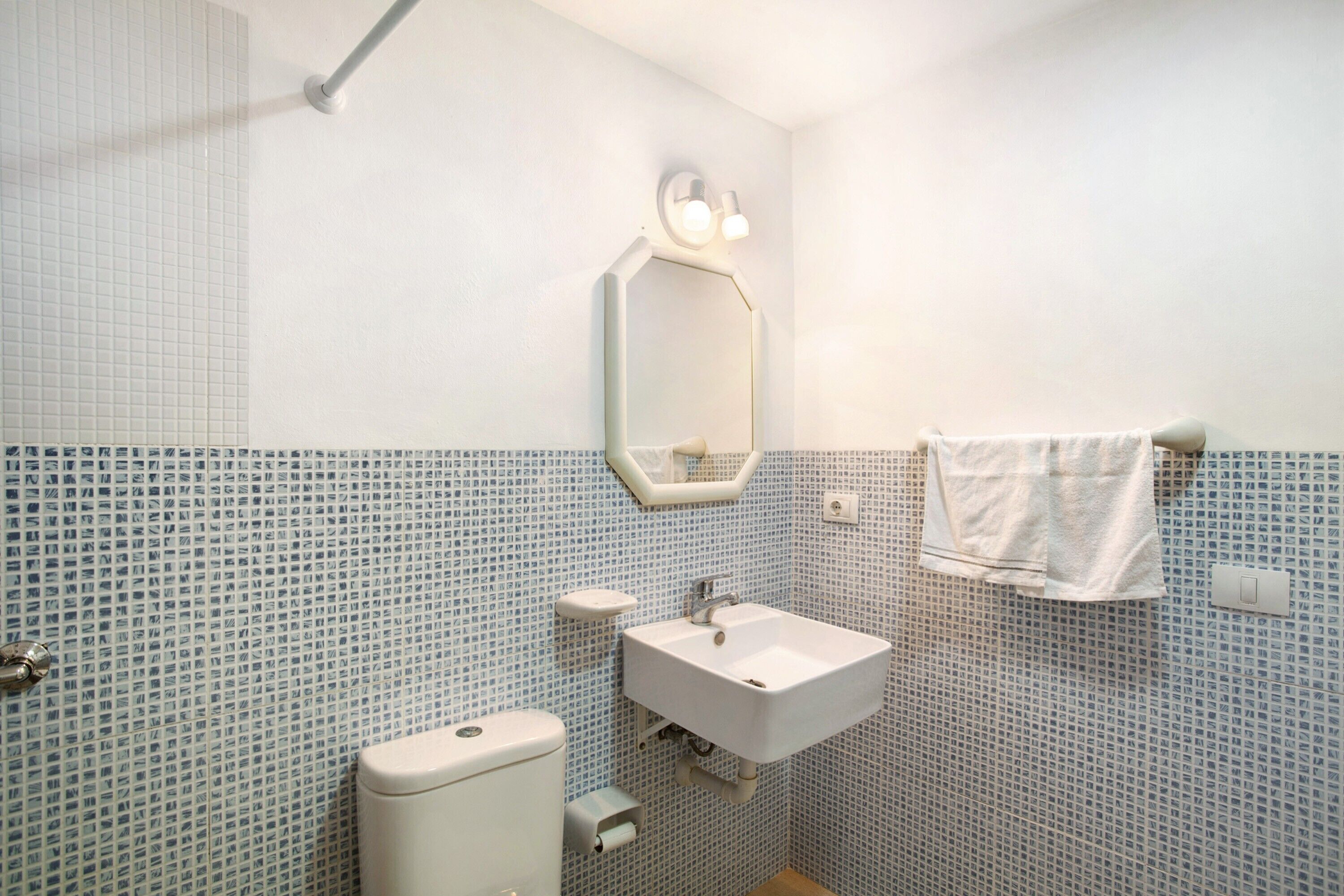 Un baño con inodoro, lavabo, espejo y toalla colgada en la pared.