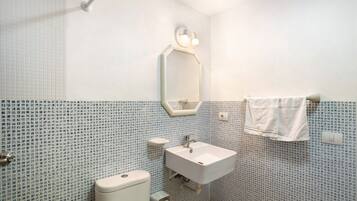 Un baño con inodoro, lavabo, espejo y toalla colgada en la pared.