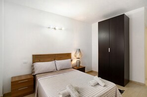 Ein Schlafzimmer mit Bett, Nachttischen, einer Lampe, einem Kleiderschrank und einer Wandleuchte.