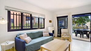Una sala de estar moderna con un sofá, una mesa, una silla y vistas a un espacio exterior a través de un ventanal.