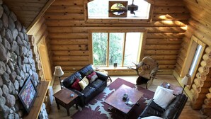 A log cabin interior with a stone wall, wooden furniture, and a large window.