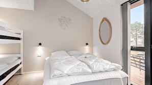 Une chambre avec un lit superposé, un grand lit avec une literie blanche, un miroir fixé au mur et une vue sur l’extérieur grâce à une porte coulissante.