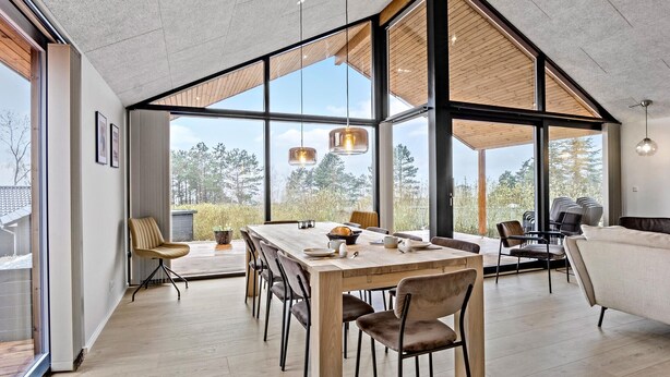 Un vaste espace d édié à la salle à manger, avec une longue table en bois, de nombreuses chaises et de grandes fenêtres donnant sur l’extérieur.