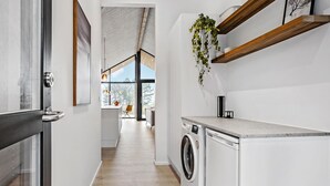 Une cuisine moderne équipée d’un lave-linge, d’une étagère en bois et donnant sur un coin repas.