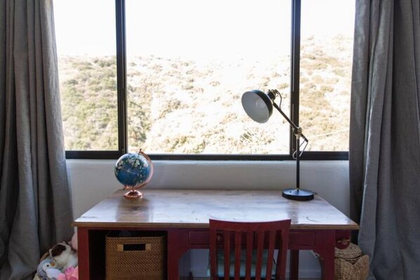 A desk with a globe and a lamp, a chair, and a view of a desert landscape through a window. - Panoramic View 5BR/3Bath Pool Private Tennis Court (Malibu)