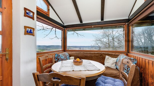 A cozy room with a round wooden table, two chairs, and a bench with cushions. There are two windows offering a view of the countryside. - Lovely home in Veliki Grdevac with WiFi (Veliki Grdevac)