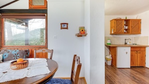 A cozy dining area with a wooden table, chairs, and a window overlooking greenery. A small kitchen with wooden cabinets and a refrigerator is visible in the background. - Lovely home in Veliki Grdevac with WiFi (Veliki Grdevac)