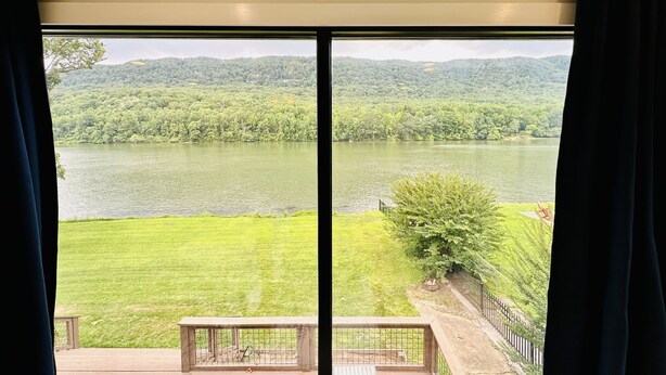 Una habitación con un ventanal grande que da a un lago y colinas boscosas.
