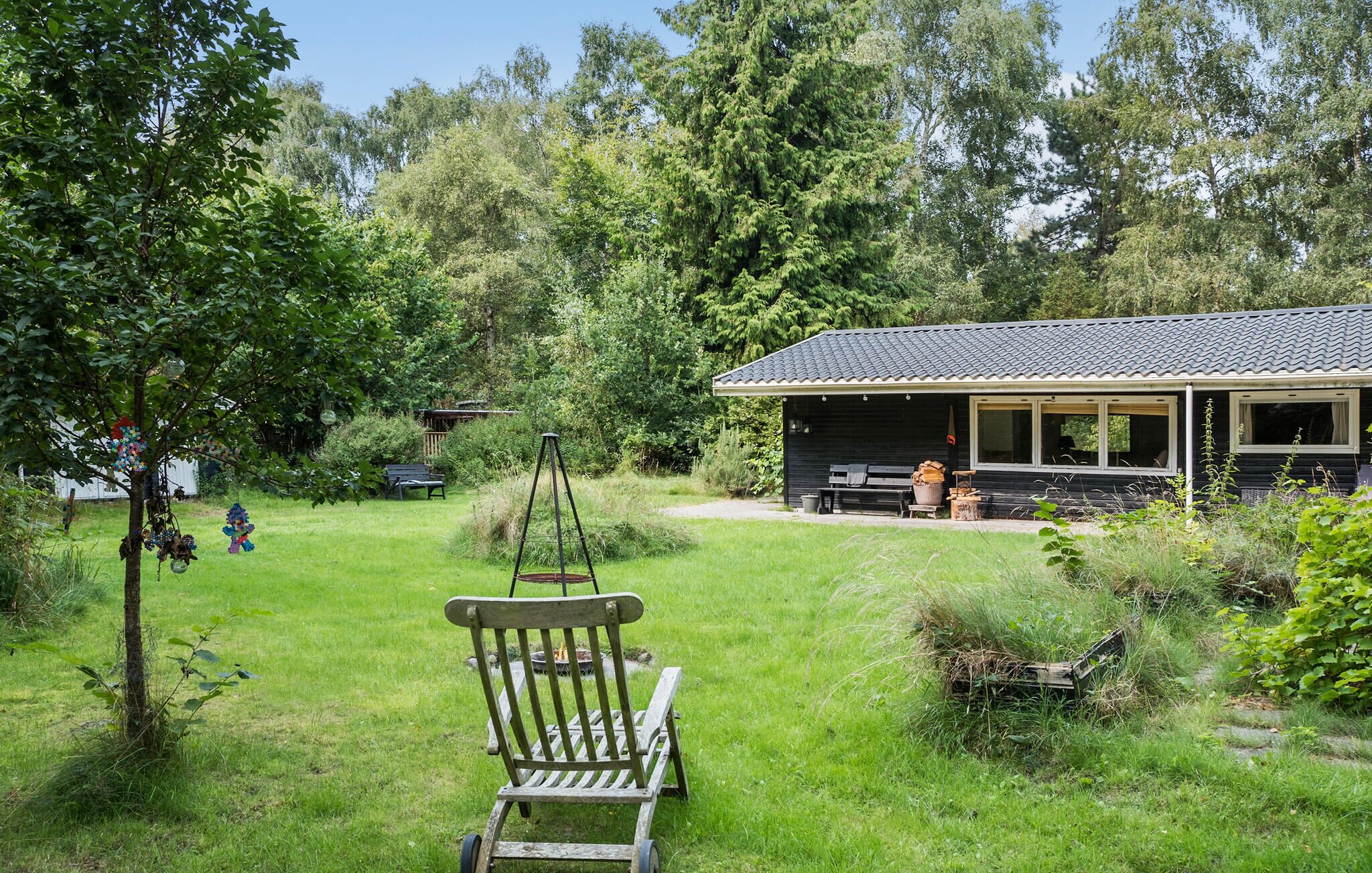Un chalet rustique doté d’un porche, entouré d’une végétation luxuriante et agrémenté d’une chaise suspendue.