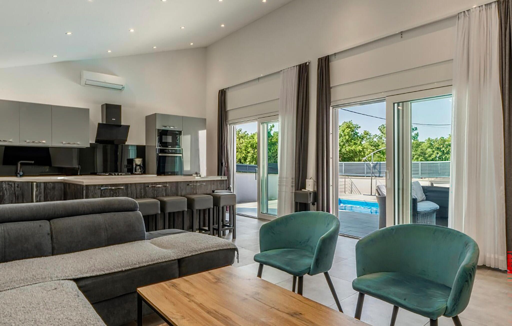 A modern living room with a sofa, a coffee table, and two chairs. There is a kitchen area with cabinets and appliances.