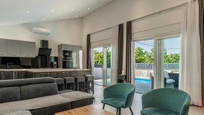 A modern living room with a sofa, a coffee table, and two chairs. There is a kitchen area with cabinets and appliances. - Amazing home in Kraljevica (Kraljevica)