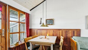 Un comedor con una mesa y sillas de madera, una ventana con cortinas rojas y una lámpara colgante fijada a la pared.