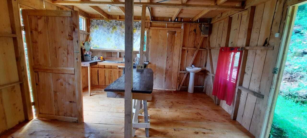 Une cabane en bois rustique dotée d’un coin cuisine comprenant un banc, un évier et une fenêtre.