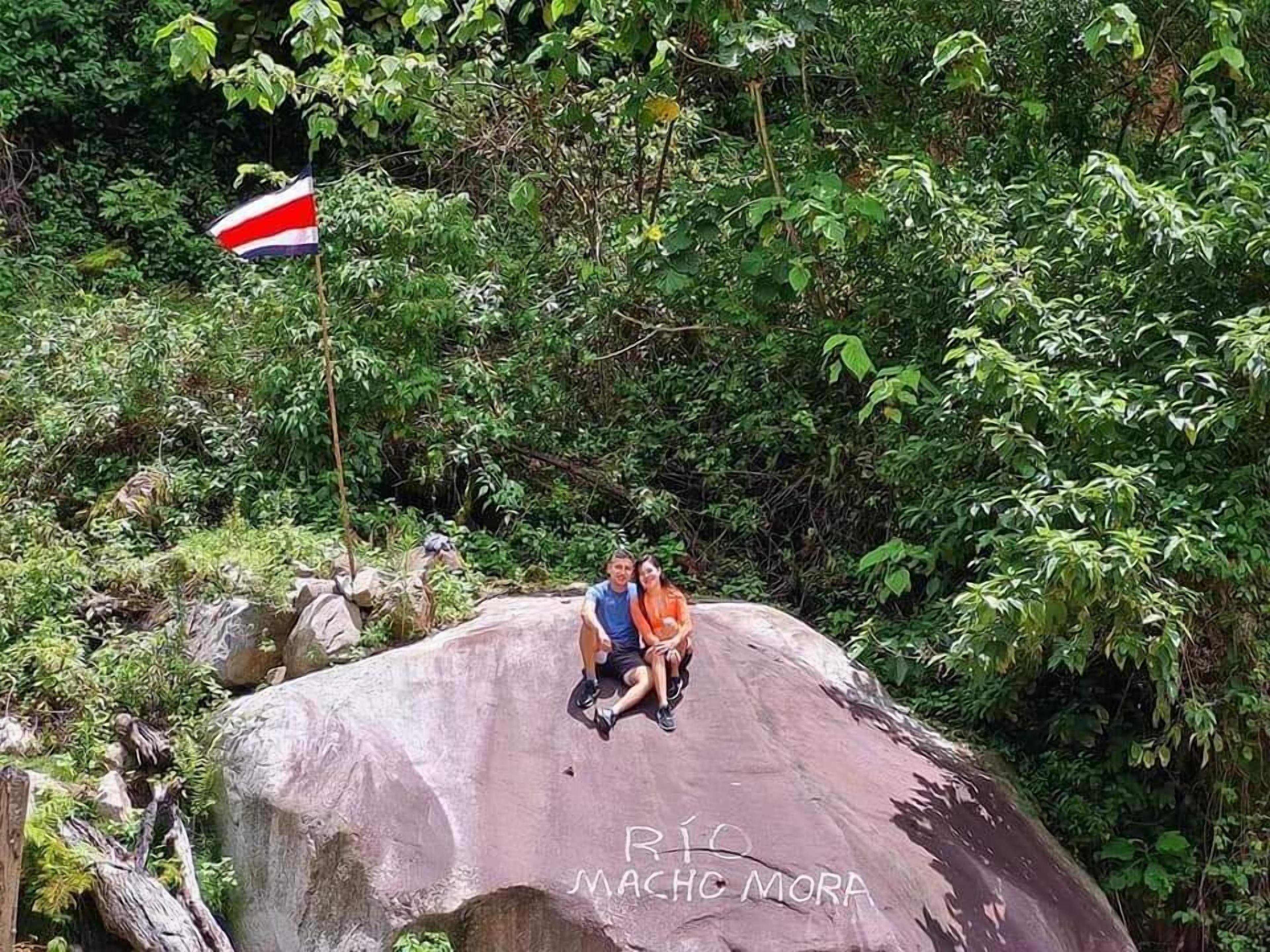 A couple sitting on a large rock with a flag in the background.