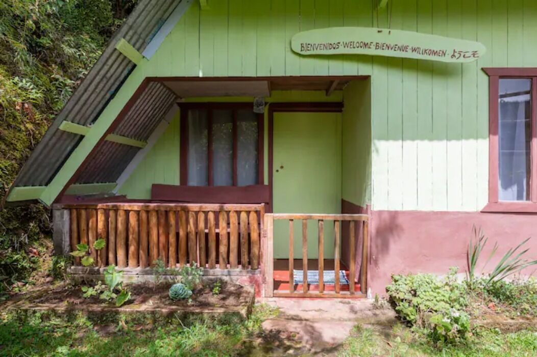 A small, green building with a wooden porch and a sign that reads "BIENVENIDOS-WELCOME-WELKOMEN-WILIKOMEN."