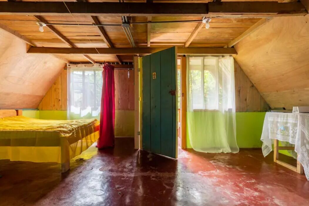 A rustic wooden room with a bed, a table with a tablecloth, and a door leading to another room.