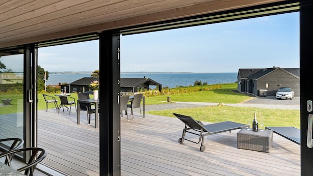 En terrass med utemöbler, utsikt över havet och en byggnad i bakgrunden.