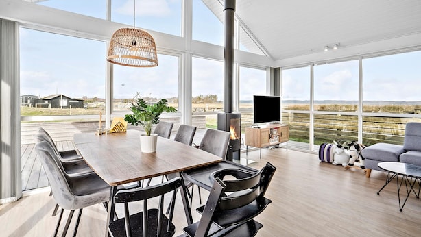 Een ruime kamer met een grote houten tafel, moderne stoelen, een hanglamp, een open haard en een televisie.