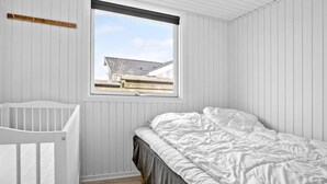 Een slaapkamer met een ledikant, een bed met wit beddengoed, een raam met uitzicht op een gebouw en witte paneelwanden.
