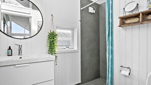 Een badkamer met witte kastjes, een spiegel, een raam, een douchegordijn en een handdoekrek.