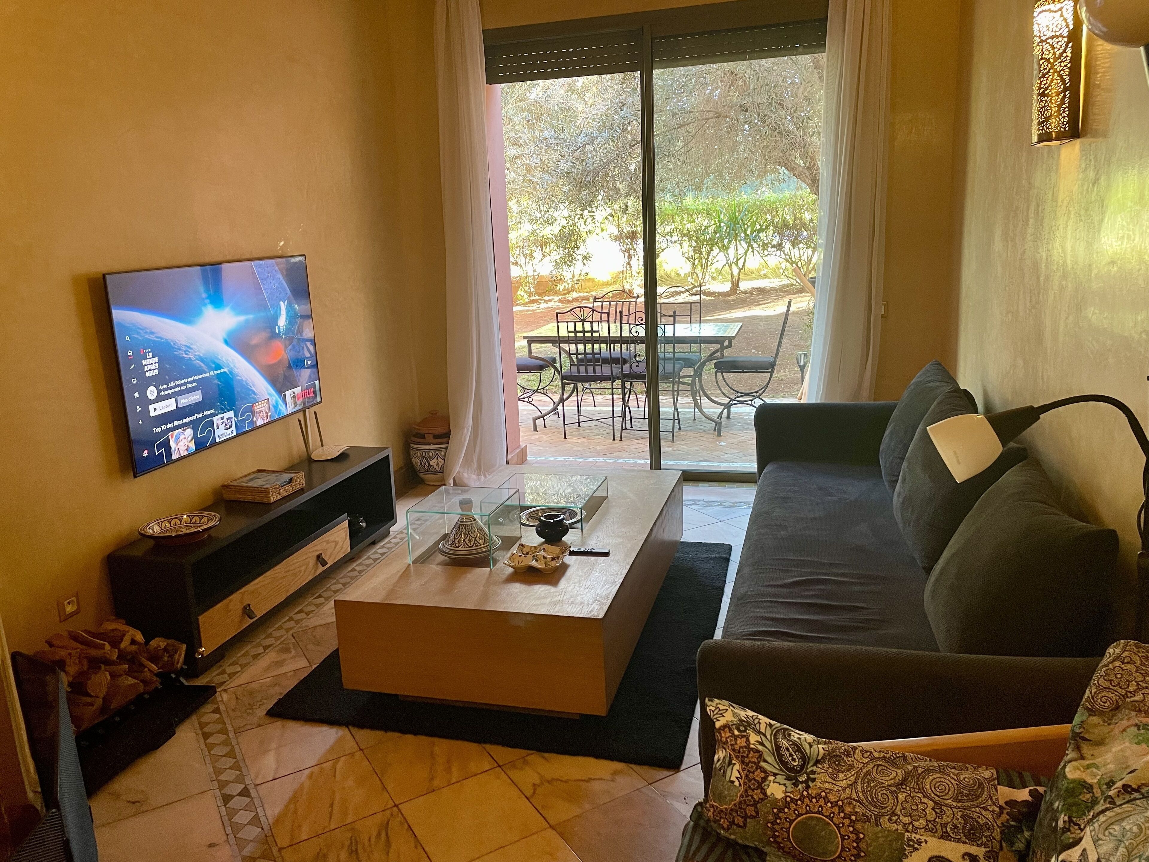 Ein Wohnzimmer mit Flachbildfernseher, einer Couch, einem Couchtisch und einem Essbereich, der durch eine Glastür sichtbar ist.