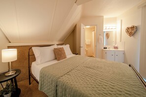 Un dormitorio con cama, mesita de noche, lámpara y vista al baño.