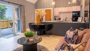 A modern kitchen with a central island, a dining area with a glass table, and a living room with a sofa and decorative pillows.