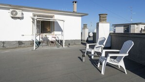 Una terraza en la azotea con sillas blancas, una mesa y una puerta abierta que da a una habitación.