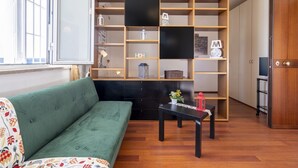 Una habitación con un sofá verde, una estantería de madera, una mesita con una planta y un armario.
