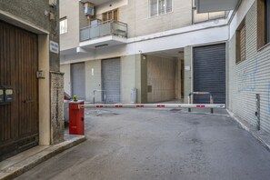 Une cour fermée par un portail, avec des portes à volets clos, un extincteur rouge et un mur en pierre.