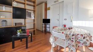 Una habitación con una estantería de madera, un televisor de pantalla plana, una mesa de comedor con mantel floreado y un cartel que dice 'PARTY ZONE'.