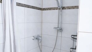 A shower with a handheld showerhead and a wall-mounted faucet.