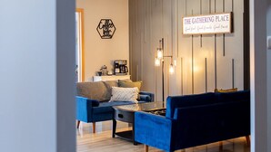 A modern living room with a blue sofa set, a coffee table, and a wall-mounted sign reading "The Gathering Place". - Rare Super Host - Arcade w/ 5 Kings, Hot Tub, Pub (Inver Grove Heights)