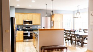 A modern kitchen with wooden cabinets, stainless steel appliances, and a dining area with a bench and chairs. - Rare Super Host - Arcade w/ 5 Kings, Hot Tub, Pub (Inver Grove Heights)