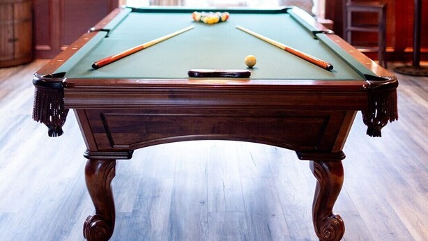 Une table de billard dans une pièce dont le sol est en bois et dont le plafond est décoré.