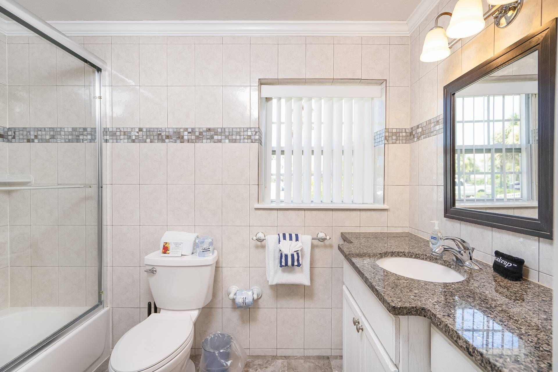 A bathroom with a toilet, bidet, and bathtub. There is a window with blinds, a sink with a mirror, and a towel rack.