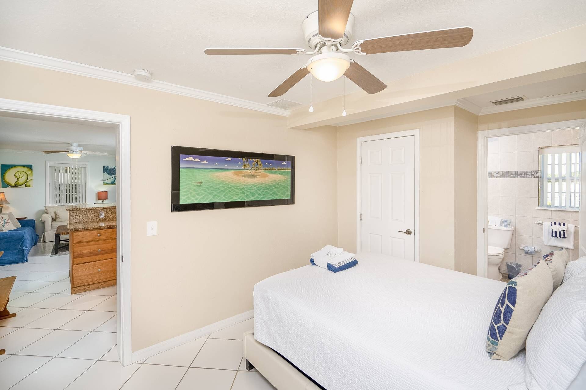 A bedroom with a bed, a ceiling fan, a TV on the wall, and a bathroom with a toilet and sink.