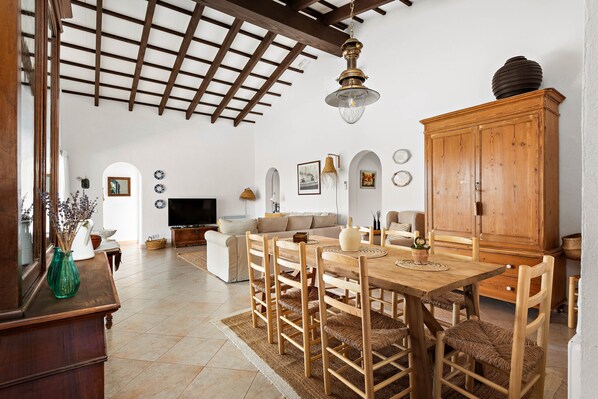 A spacious living room with a wooden dining table, chairs, and a large cabinet.