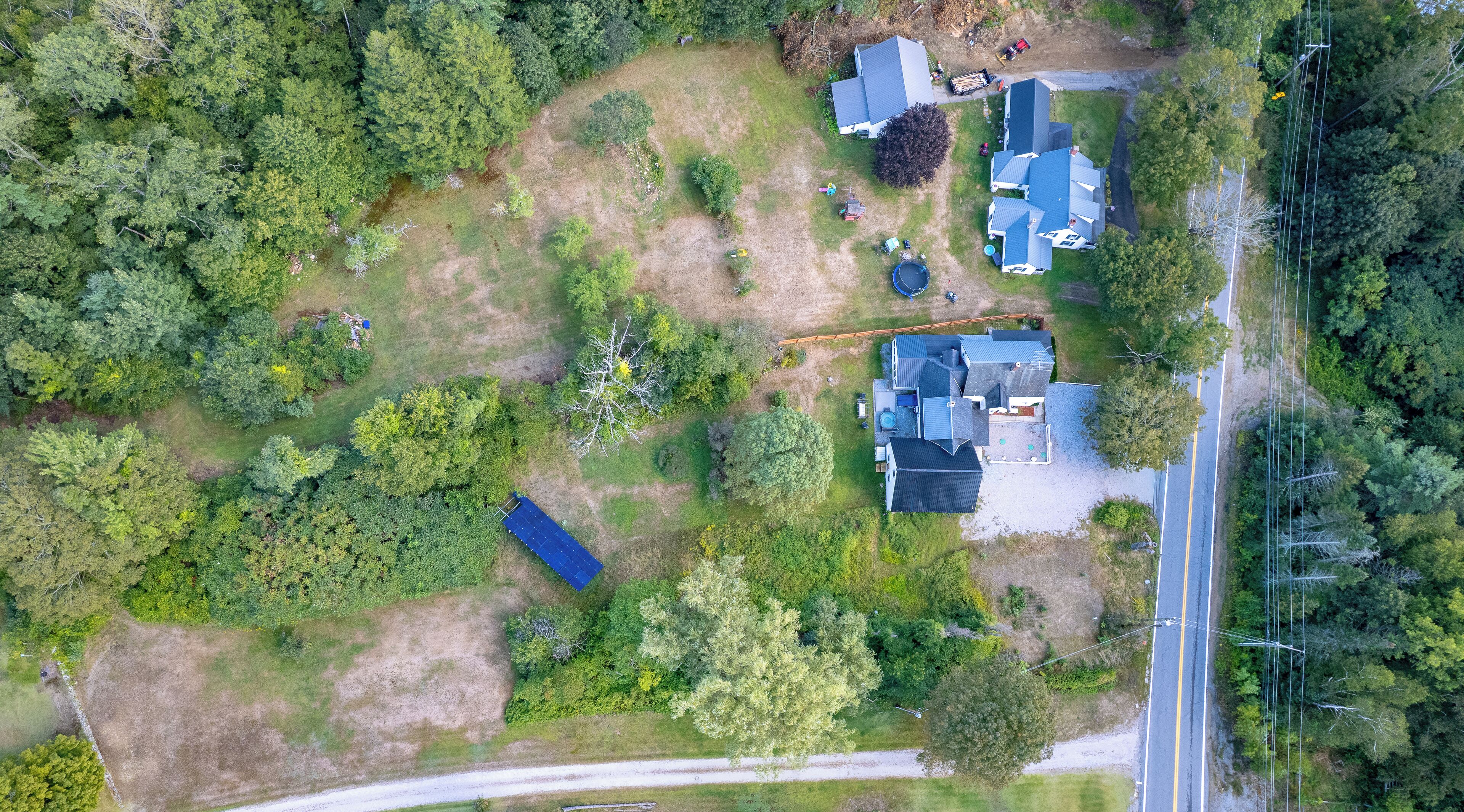 An aerial view of a residential area with multiple houses, a road, and surrounding greenery.