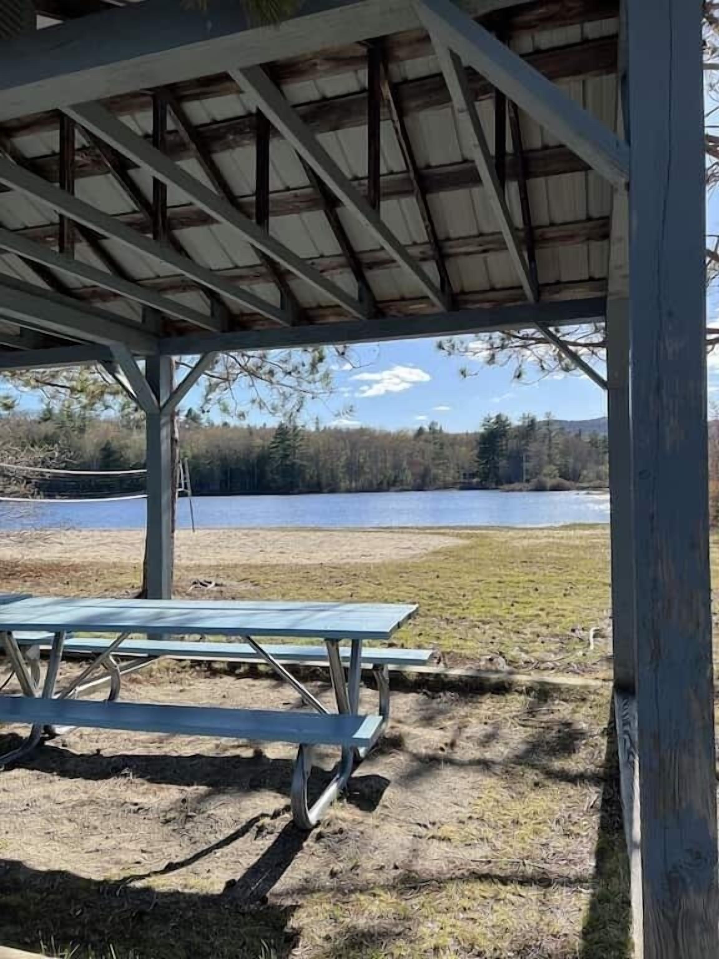 A covered picnic area with a table and benches, overlooking a lake and forested area.