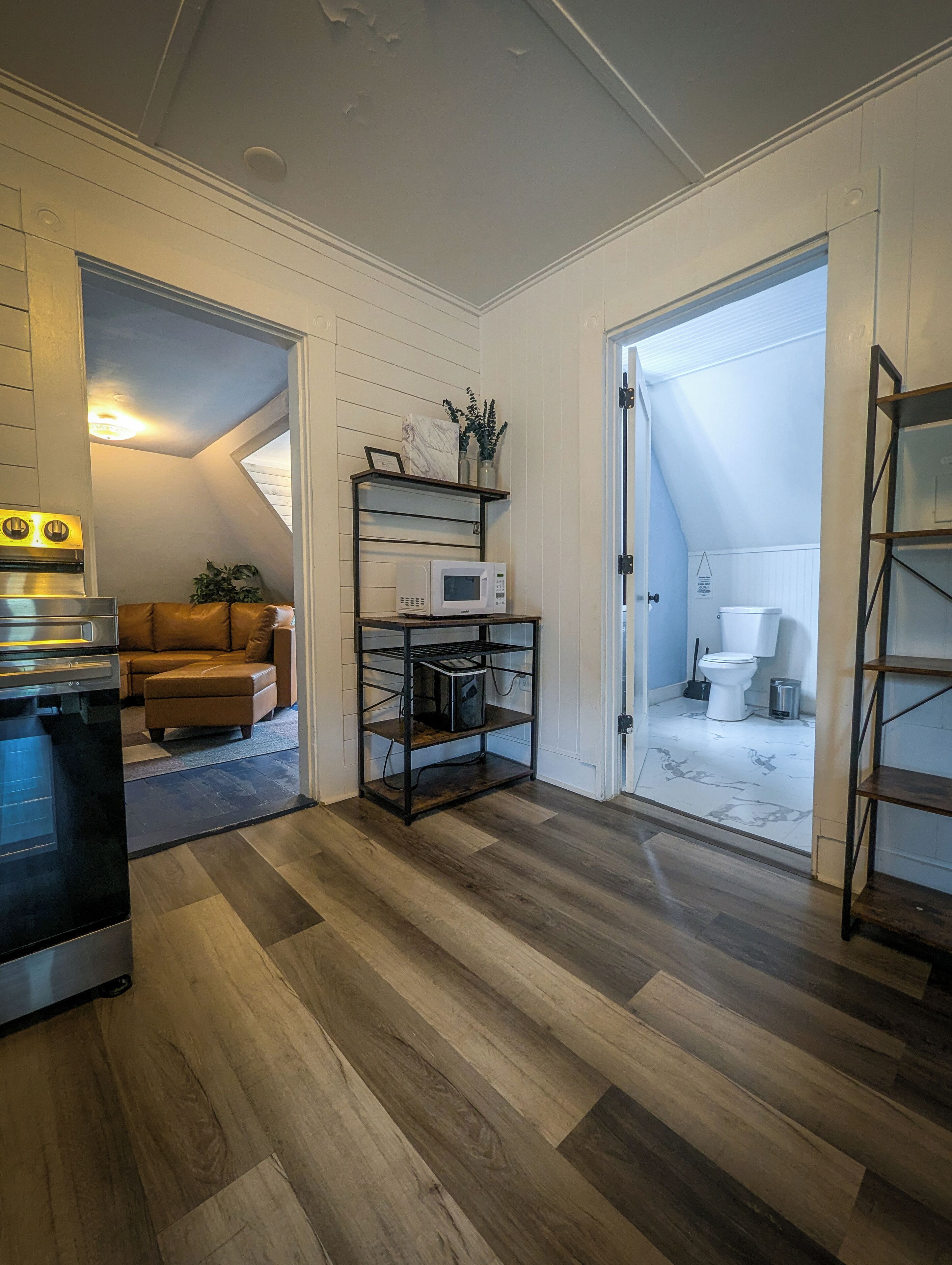 A modern kitchen with a microwave, oven, and a black countertop. There is a wooden floor and a white ceiling.
