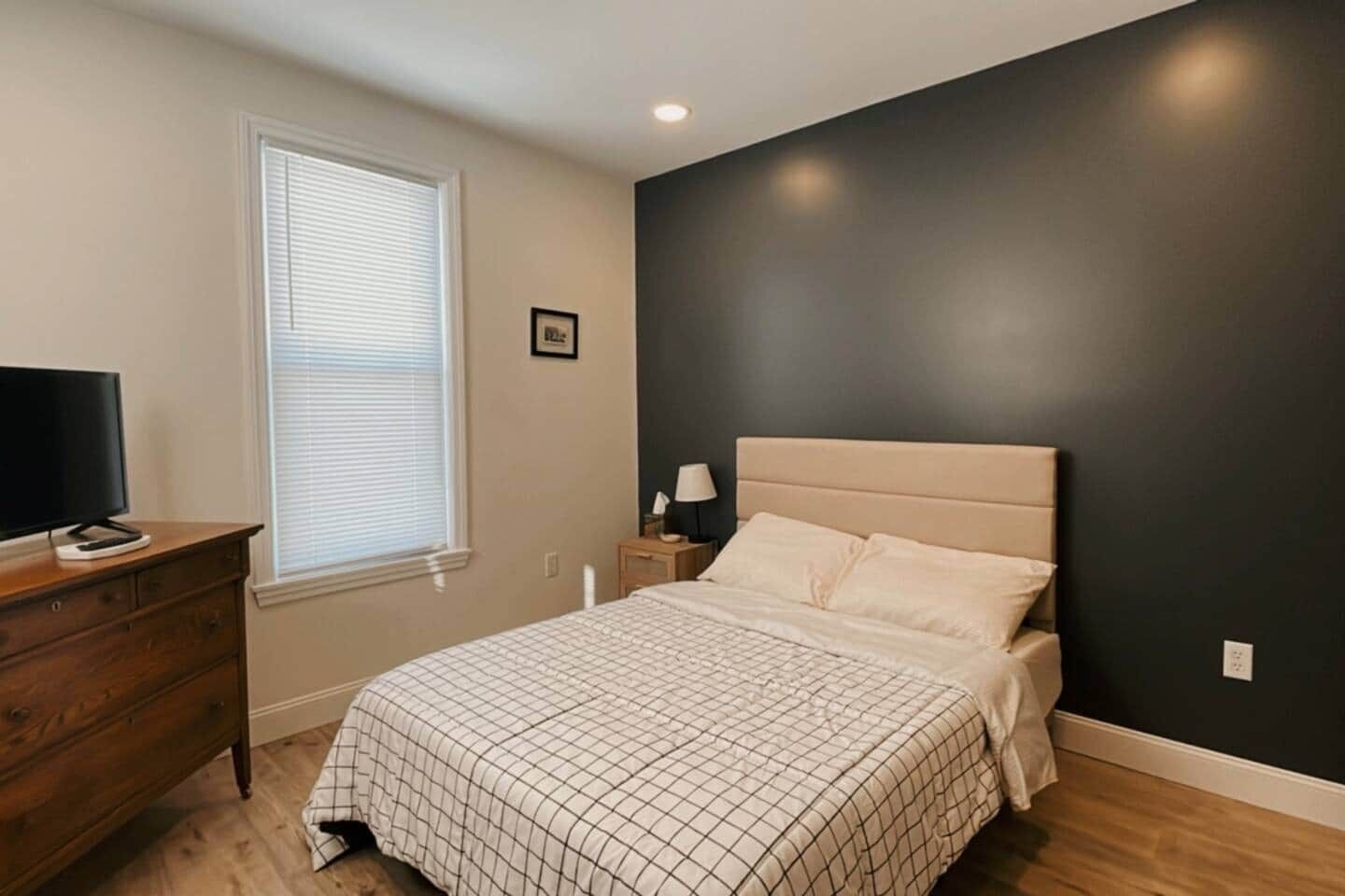 A bedroom with a bed, dresser, nightstand, lamp, and a television.