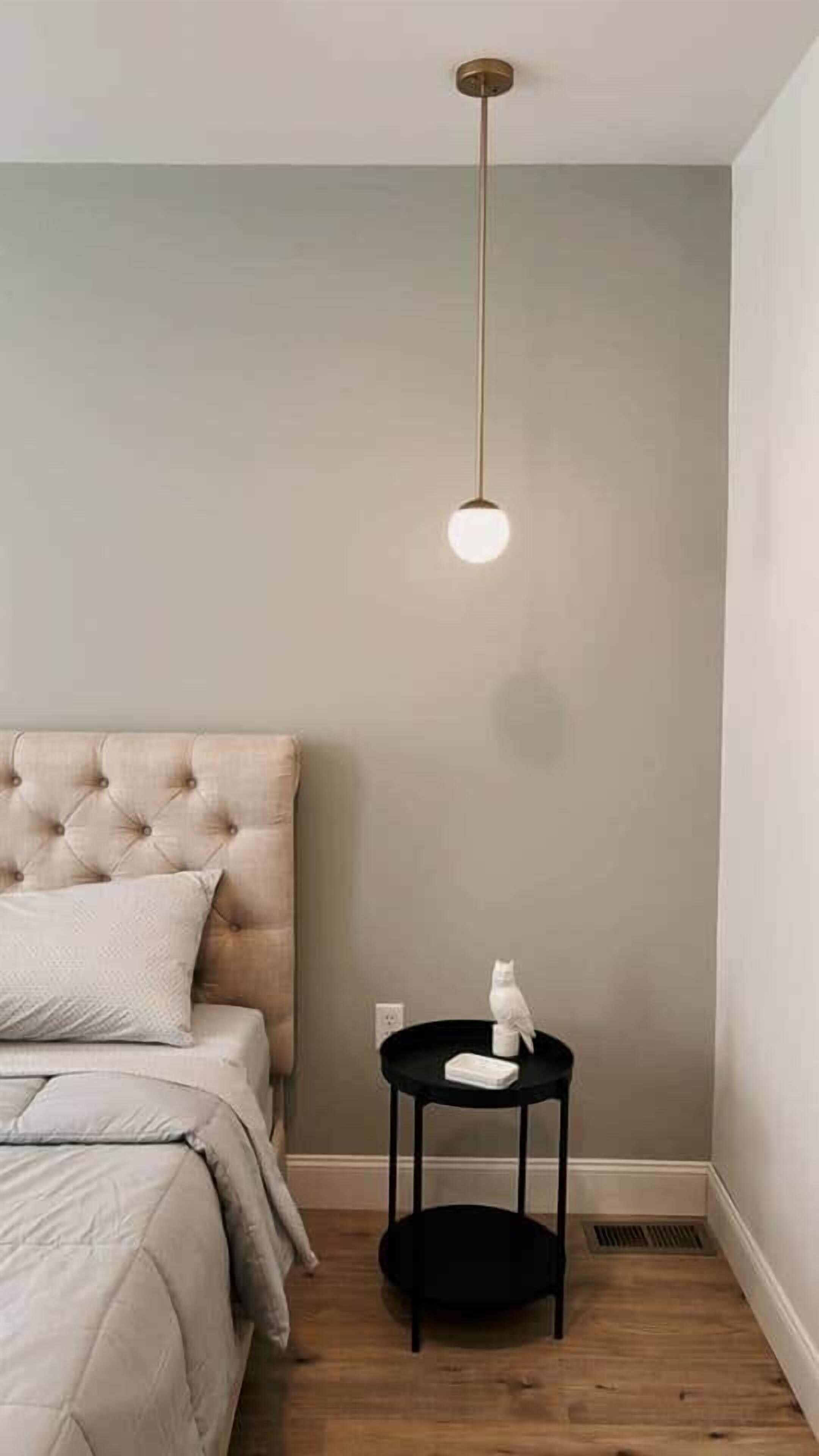 Ein Schlafzimmer mit einer gesteppten Kopfteil, einem runden Tisch mit einer weißen Skulptur und einer Pendelleuchte.