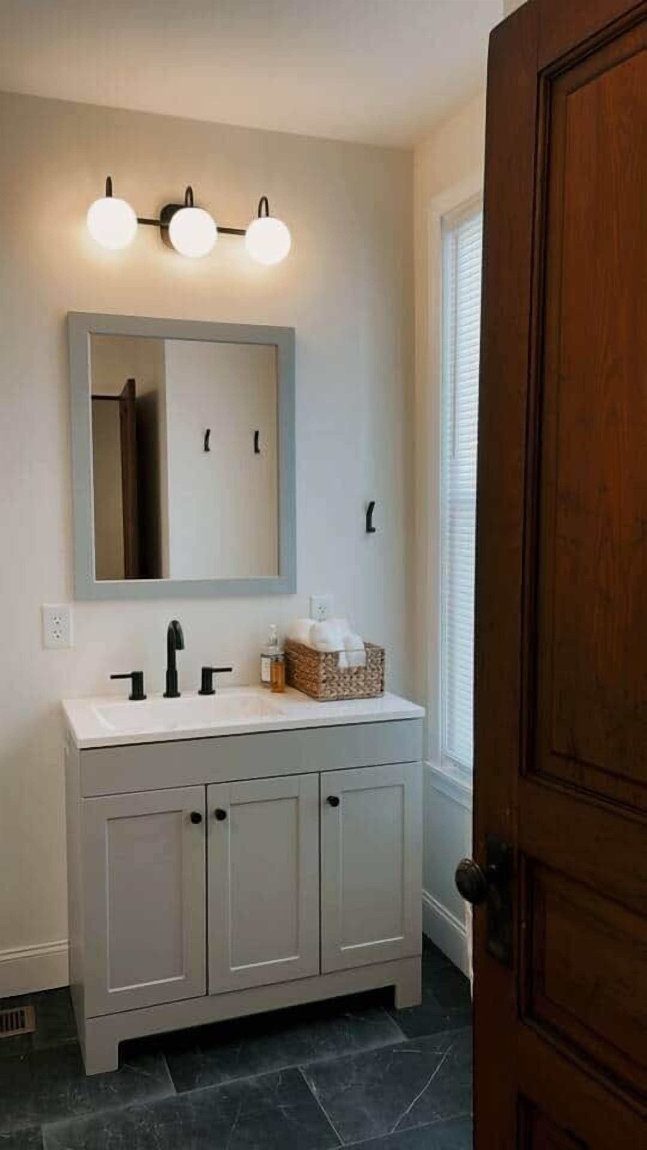 A bathroom with a white vanity, a mirror, and a light fixture above the mirror.
