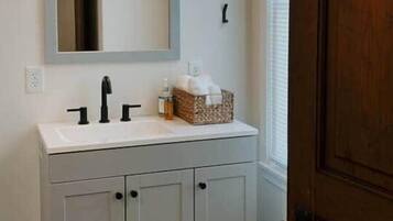 A bathroom with a white vanity, a mirror, and a light fixture above the mirror.