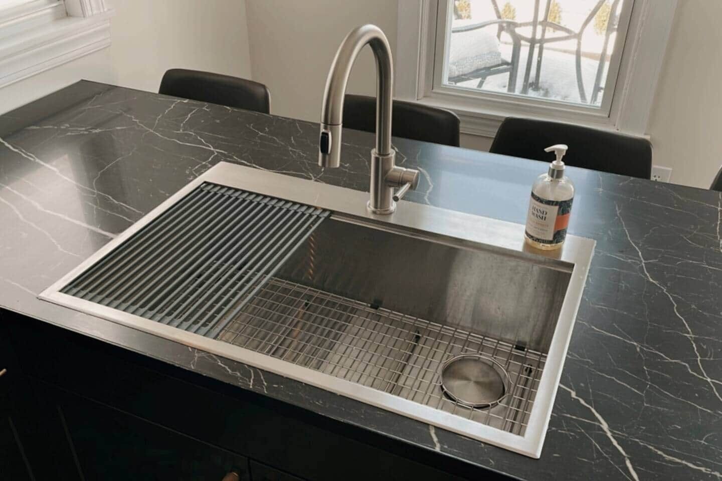 A kitchen with a stainless steel sink, a ventilation hood, and a bottle of hand soap on the counter.