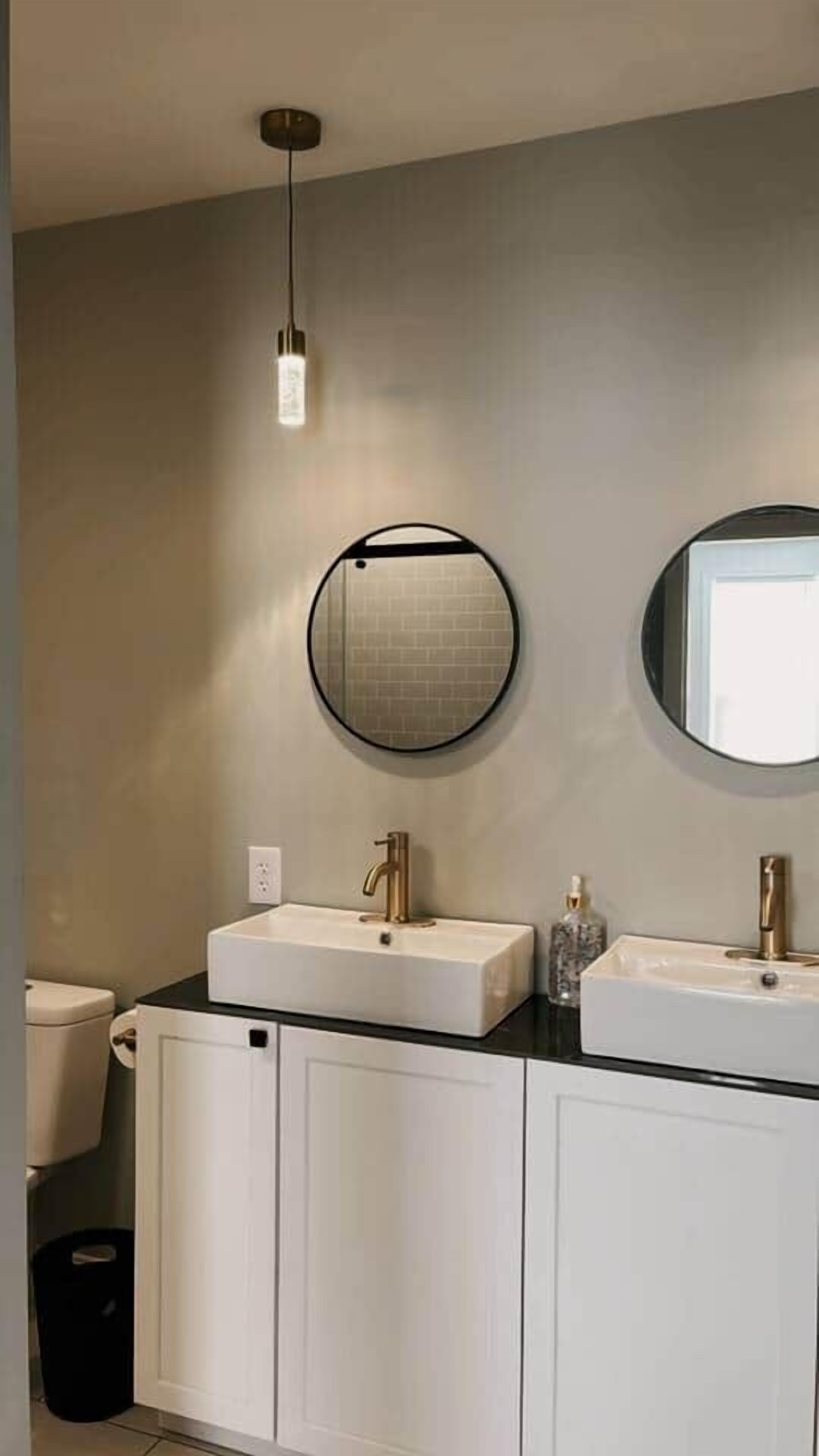 A bathroom with two sinks, a round mirror, and a light fixture.