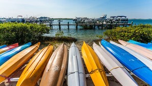 A row of canoes lined up on a sandy beach with a pier and boats in the background. - Inlet Marina Villas #524, Nestled between the River & Ocean (New Smyrna Beach)