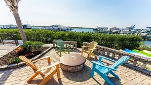 An outdoor seating area with Adirondack chairs and a round table, overlooking a marina with boats. - Inlet Marina Villas #524, Nestled between the River & Ocean (New Smyrna Beach)