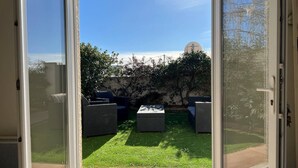 Un patio con mobiliario exterior y vistas a un jardín y un edificio al fondo.